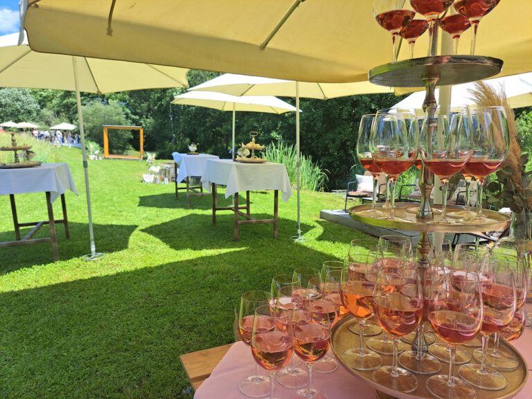 Gedeckte Stehtische und ein Rosé-Wein-Empfang unter Sonnenschirmen bei einer Sommerfeier am Fischteich des Hotel Restaurant Zollner.